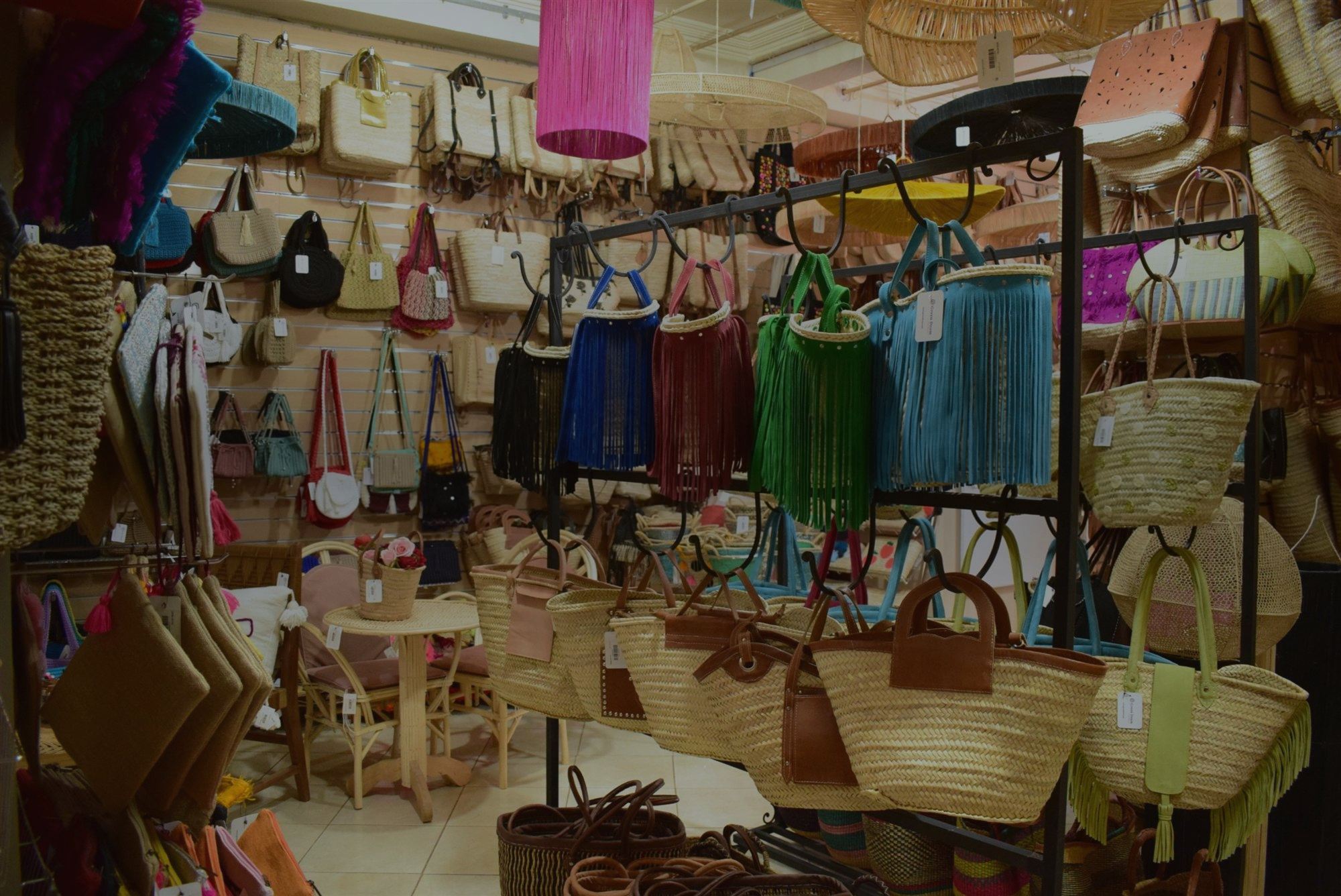 Fringed raffia and straw bags hanging beside woven baskets in the Green Doum showroom
