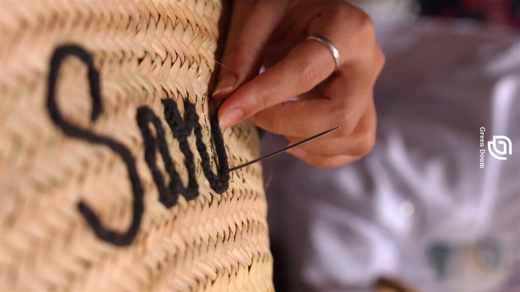 Artisan hand-stitching a name in black wool onto a Moroccan straw basket
